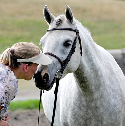 A blonde woman kissing a grey pony.
