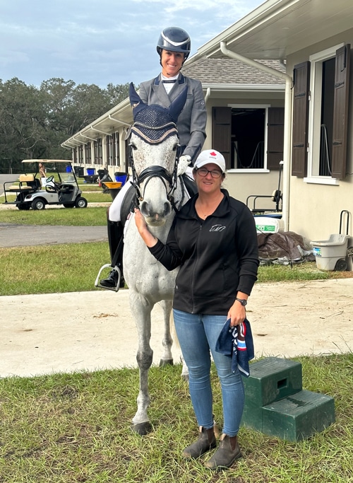 A woman on a grey horse, a woman on the ground holding the horse.