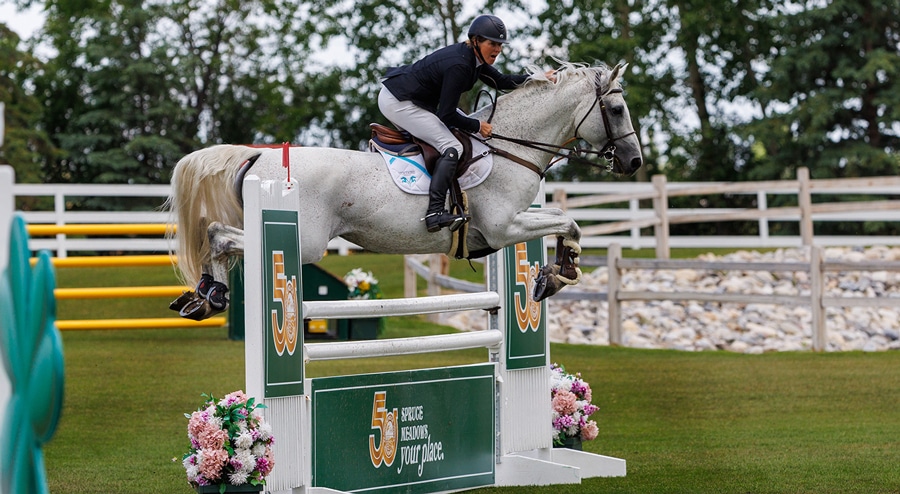 A woman jumping a grey horse over a fence at Spruce Meadows.