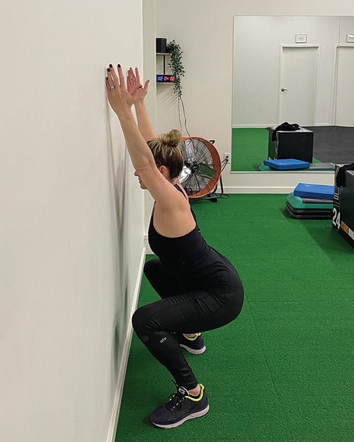 A woman squatting, facing a wall.