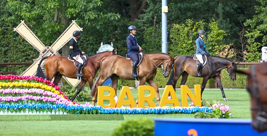 Three people on hunters walking past a 'Baran' sign.