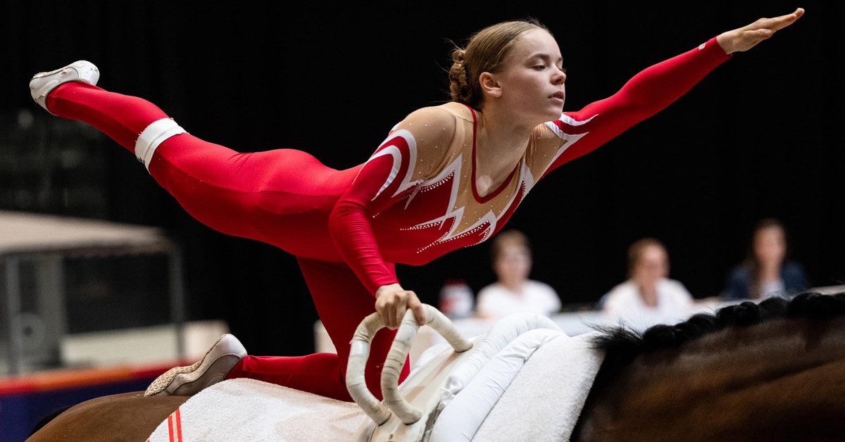 A teenage girl in a red leotard performing on a vaulting horse.