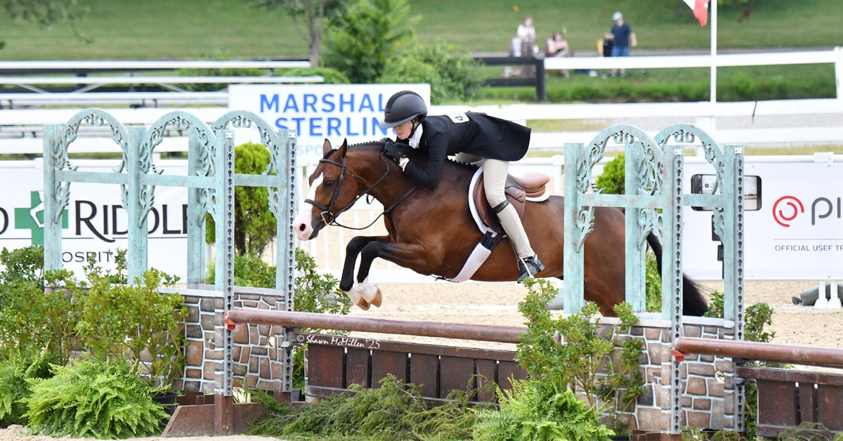 A young girl riding a pony hunter over a fence.