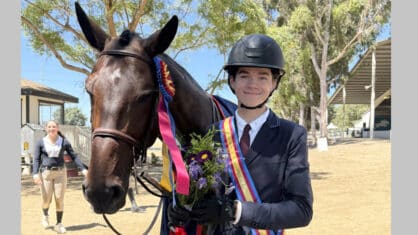 A teenage boy with a bay horse wearing a ribbon.