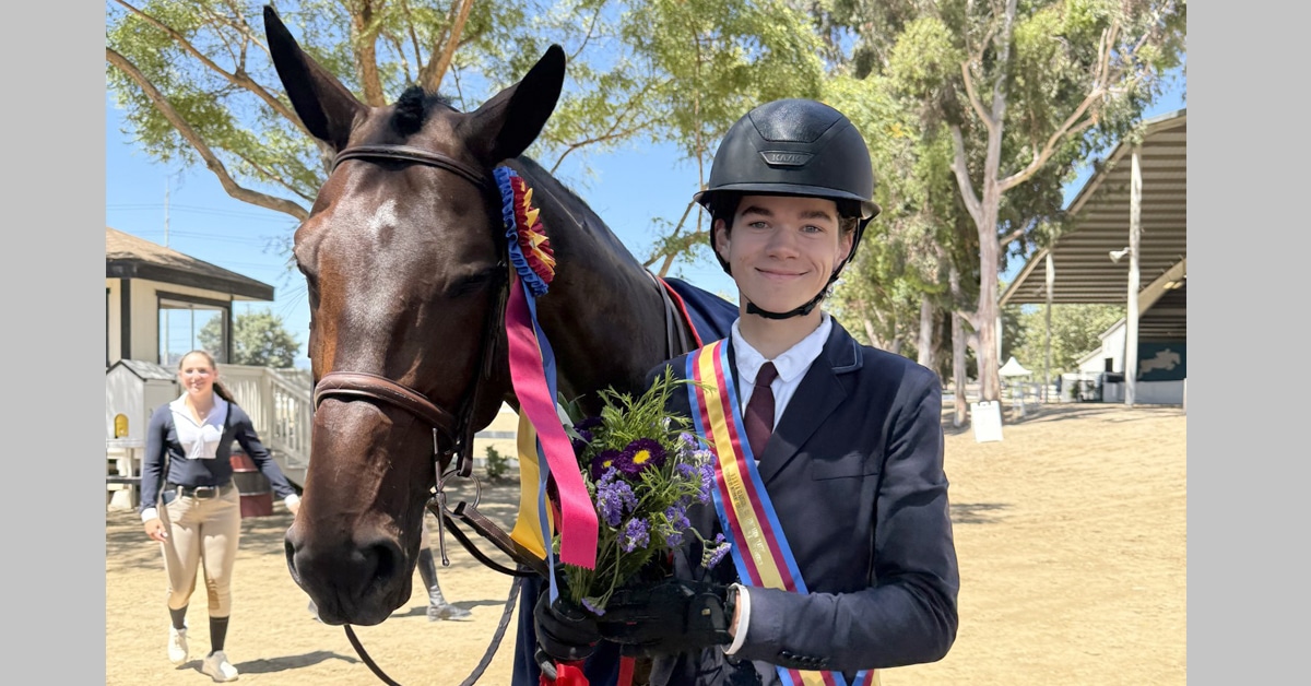 A teenage boy with a bay horse wearing a ribbon.