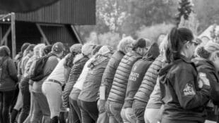 A group of riders and coaches lined up at the rail at a horse show.