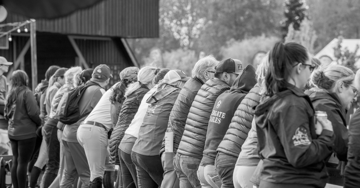 A group of riders and coaches lined up at the rail at a horse show.