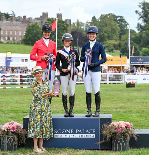 Three women on a podium with a castle behind them.
