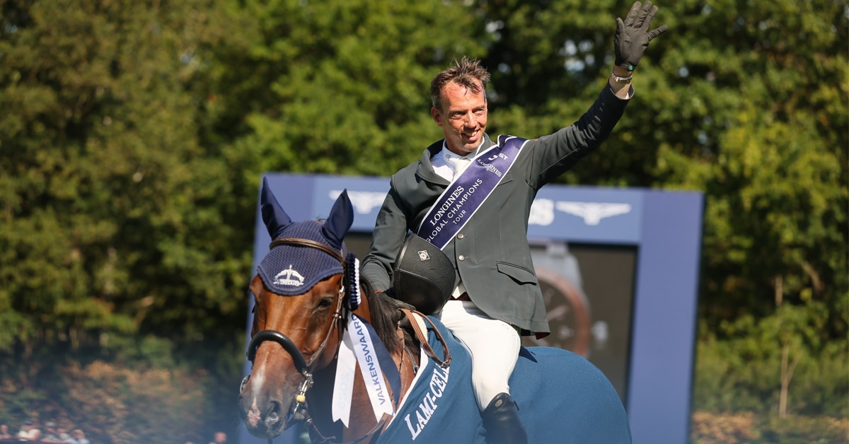 A man sitting on a bay horse, waving to the crowd.
