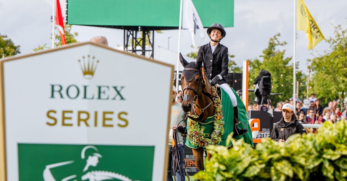 A smiling woman on a bay horse that is wearing a wreath.