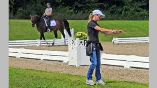 A woman standing beside a dressage ring, teaching a clinic.