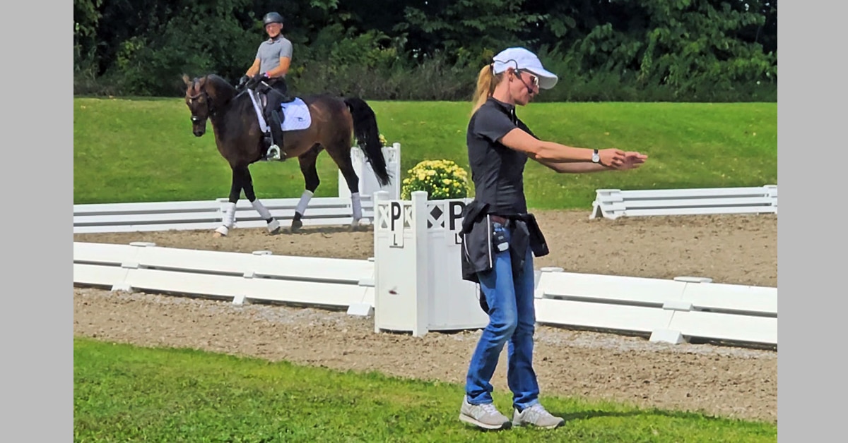 A woman standing beside a dressage ring, teaching a clinic.