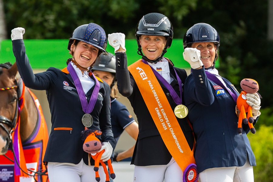 Three smiling women with medals on the podium.