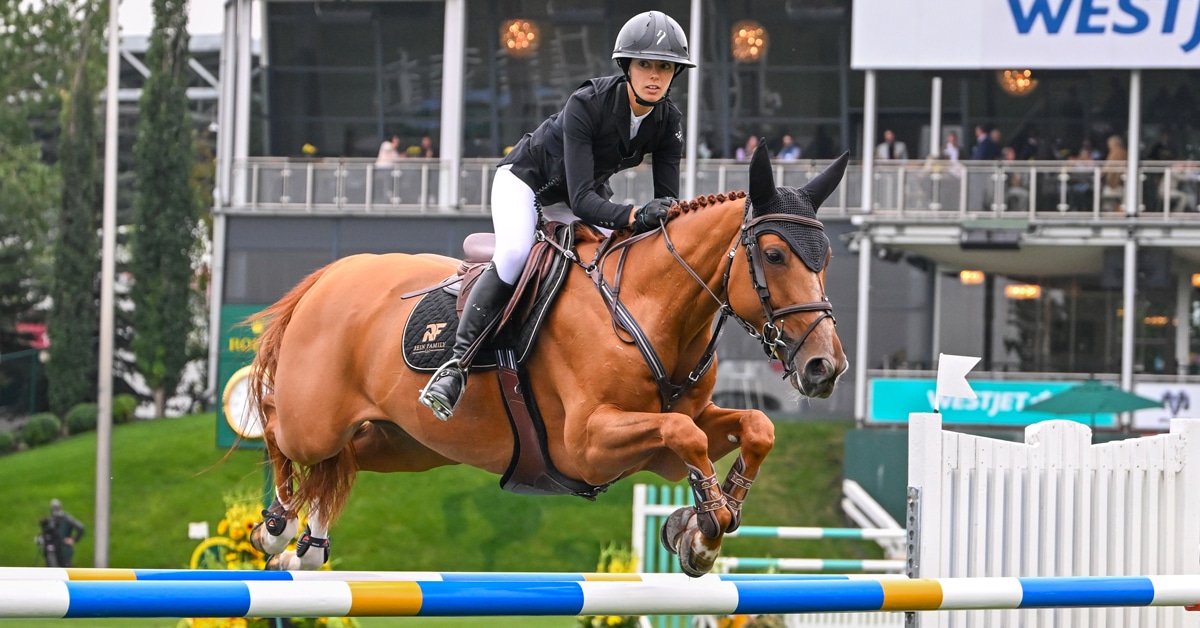 A woman jumping over a fence at Spruce Meadows on a chestnut mare.
