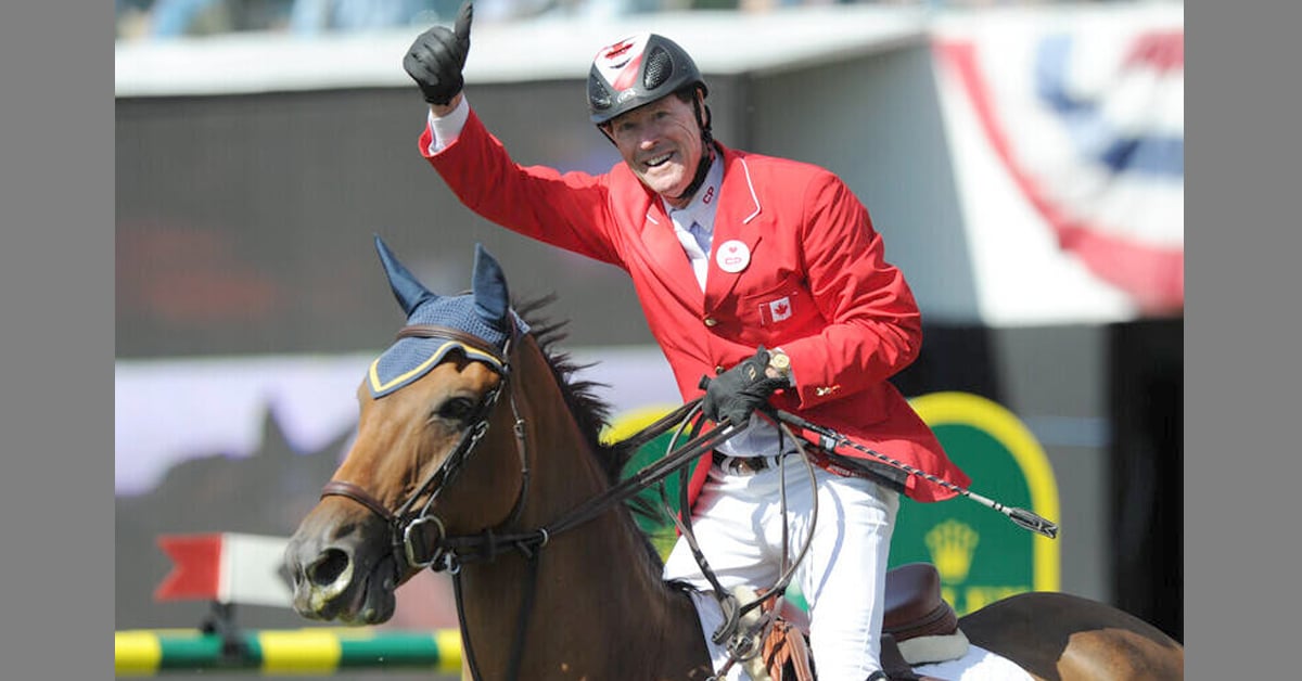 A man in a red jacket on a bay horse, waving to the crowd.