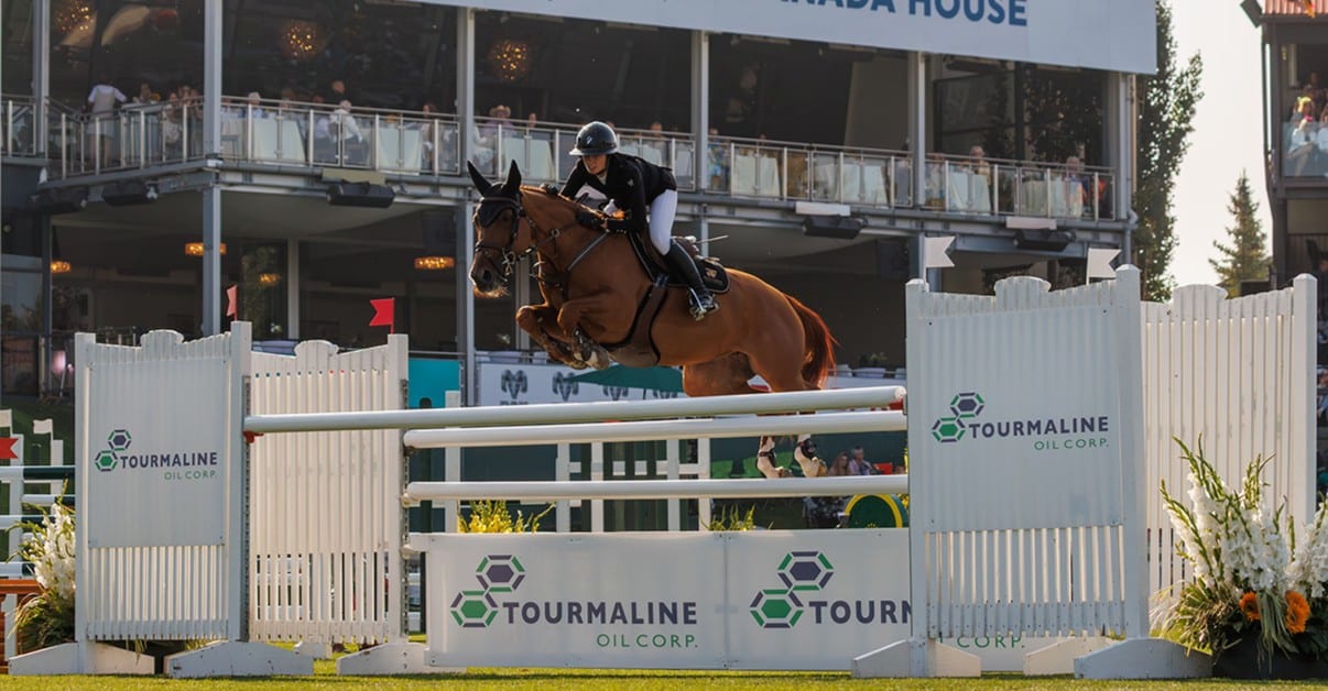 A woman riding a bay horse over a fence at Spruce Meadows.