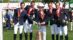 A show jumping team on a podium with a large trophy.