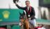 A man on a bay horse, waving his helmet in the air.
