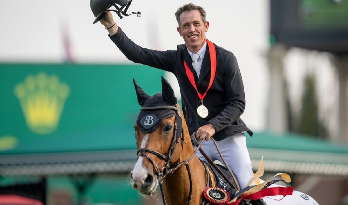 A man on a bay horse, waving his helmet in the air.