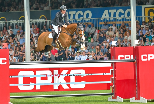 A man jumping a bay horse over a CPKC logo fence.