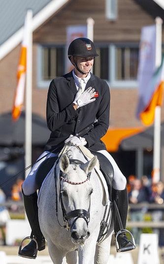 A man on a grey horse holding his hand over his heart.