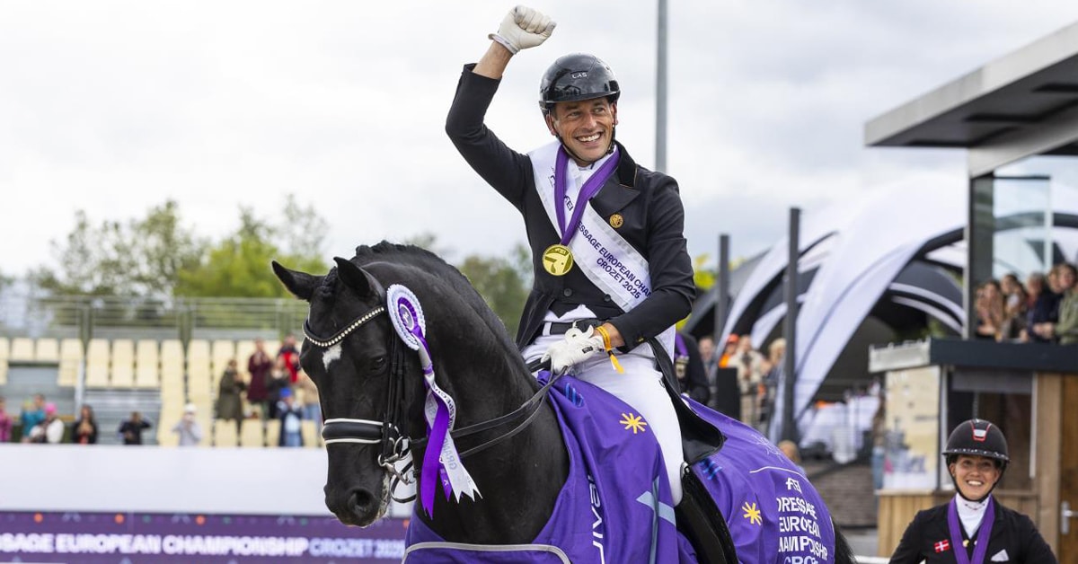 A man on a black dressage horse, waving and smiling.