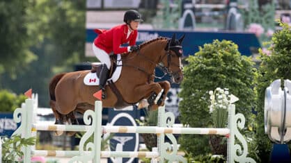 A woman in a red coat jumping a chestnut horse over a fence.