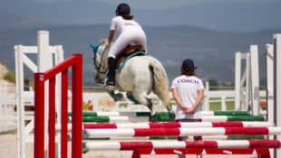 A coach watching a horse and rider jump a fence.