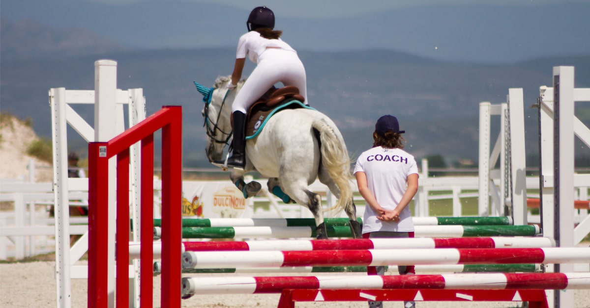 A coach watching a horse and rider jump a fence.