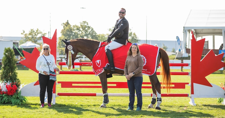 A smiling man on a bay horse during a presentation.
