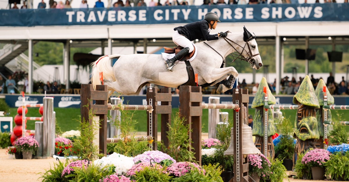 A man jumping a grey mare over a fence at Traverse City.