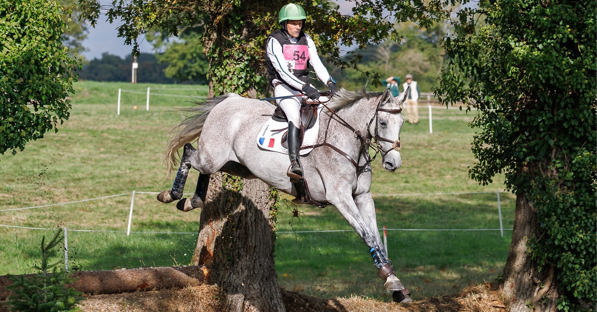 A man jumping a grey horse over a ditch at an event in France.