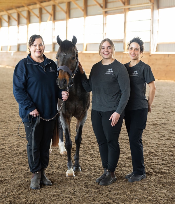 Three women standing in an arena with a horse.