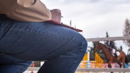 A man with a clipboard on his knee, judging a horse show class.