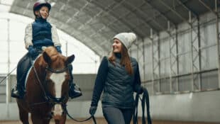 A female coach leading a young girl on a horse.