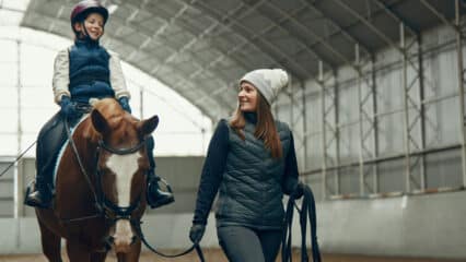 A female coach leading a young girl on a horse.