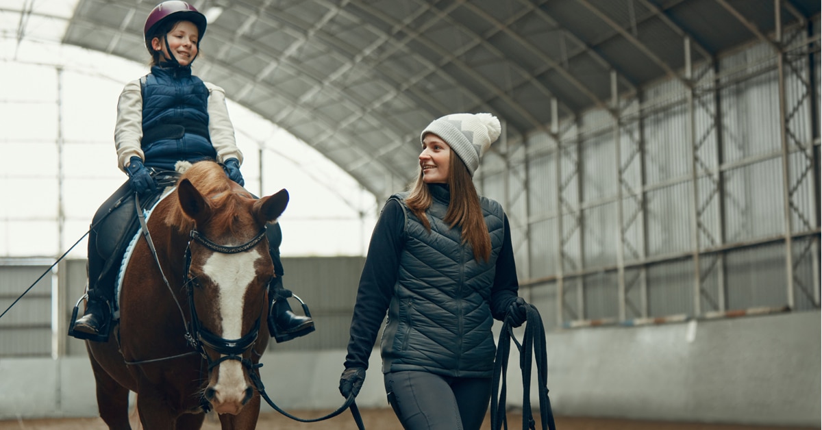 A female coach leading a young girl on a horse.