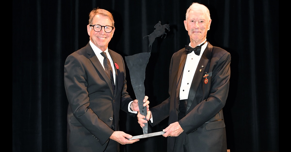 A man handing a trophy to another man in a tuxedo on a stage.