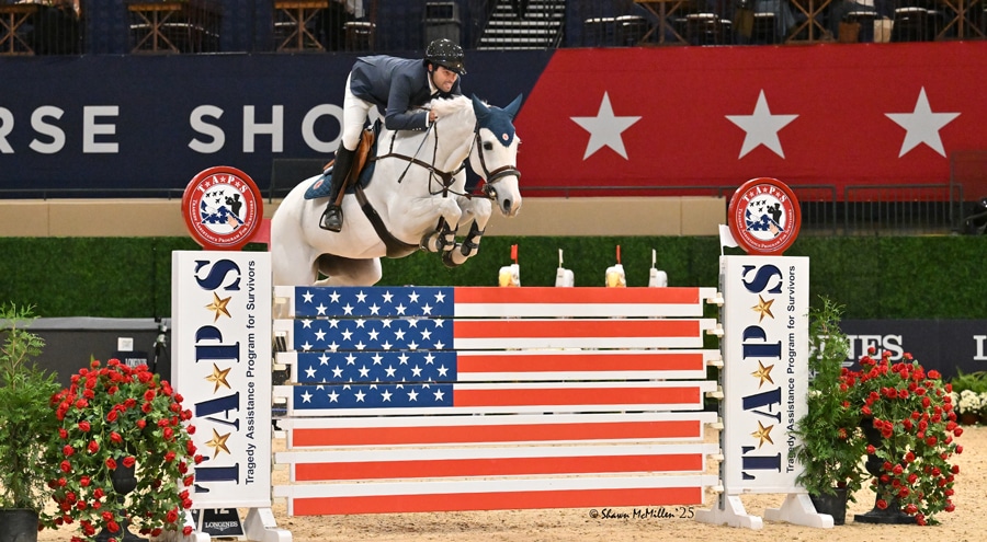 A man on a grey mare jumping a fence at an indoor horse show.