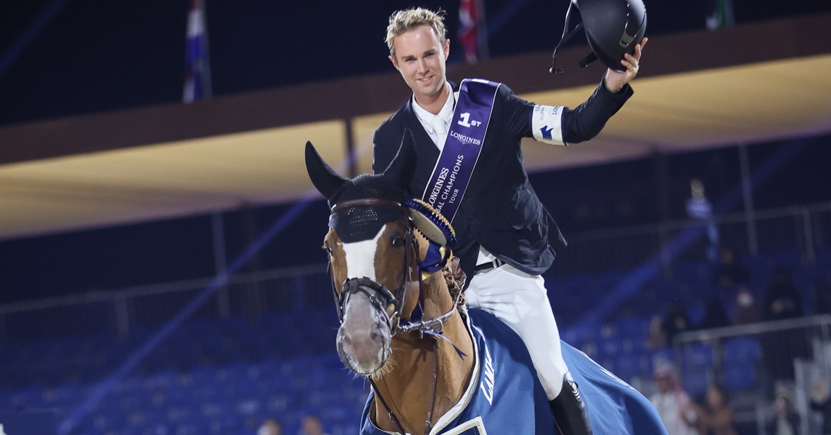 A man waving his hat, sitting on a chestnut stallion during a victory gallop.