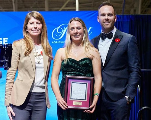 A woman holdin an award, flanked by another woman and a man.
