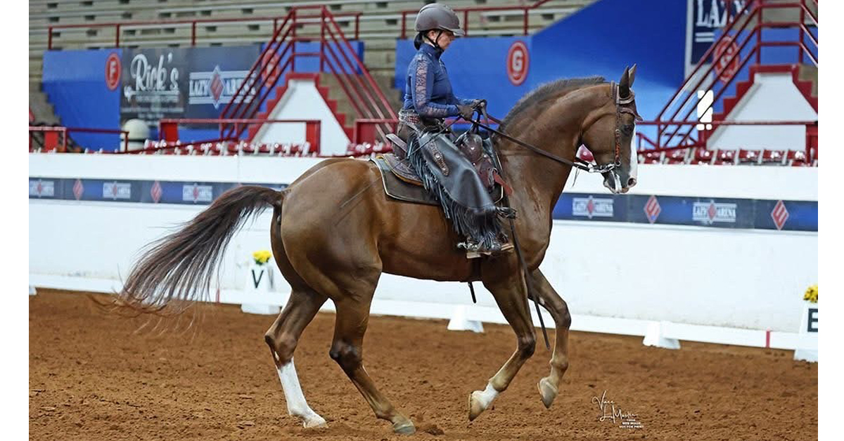 A woman on a chestnut horse performing western dressage in an arena.