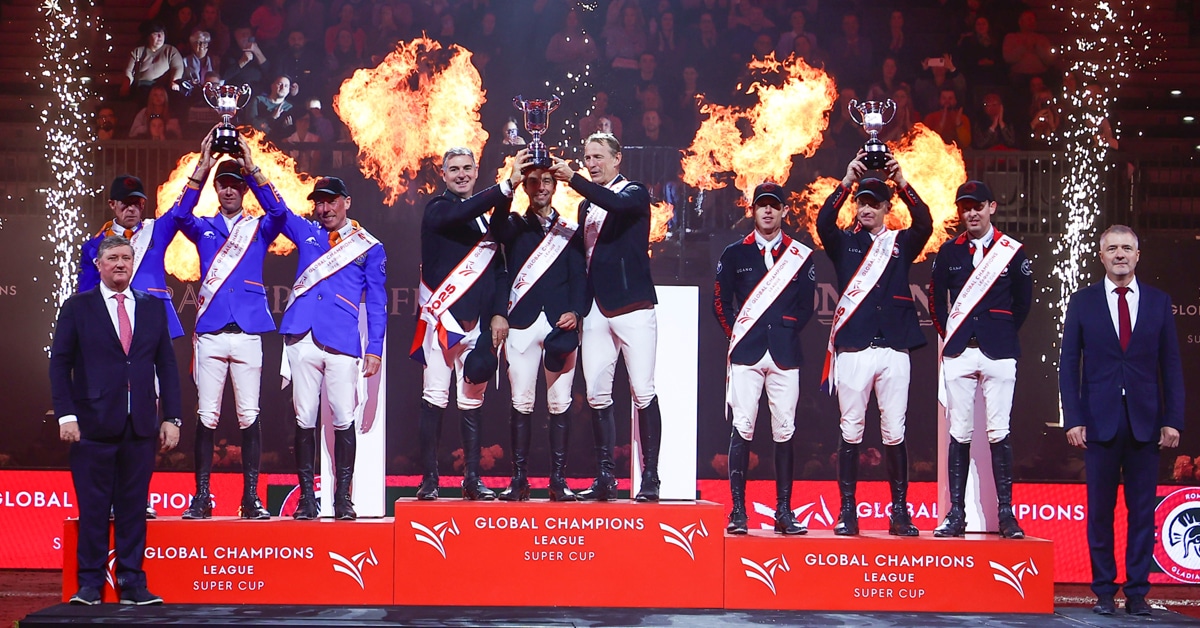 Three teams on a podium in Prague with pyrotechnics behind.