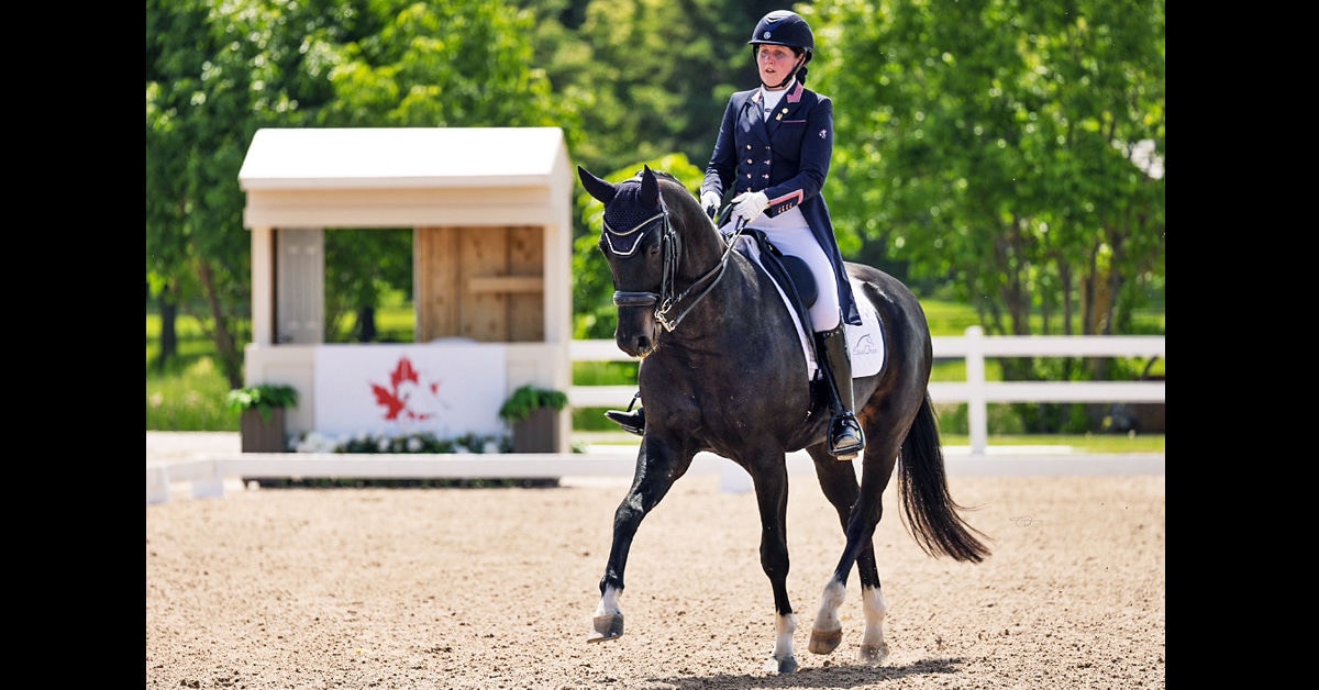 A woman riding a black dressage horse during a test.