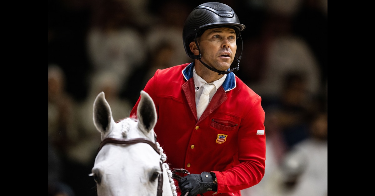 A man wearing a red jacket and riding a grey mare.