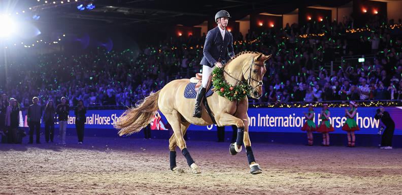 A man on a chestnut horse that is wearing a wreath.