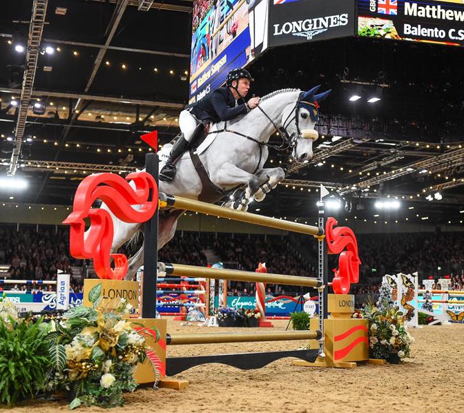 A man jumping a grey horse over a fence in London.