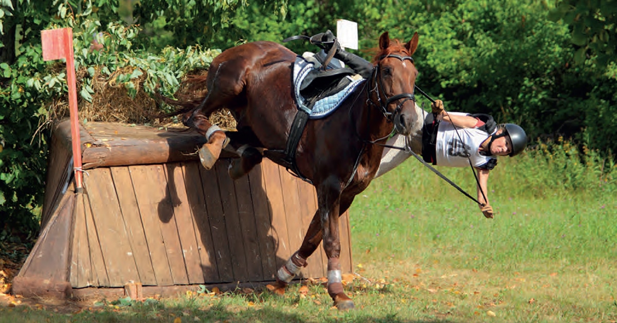 A person falling off a horse over a cross-country fence.