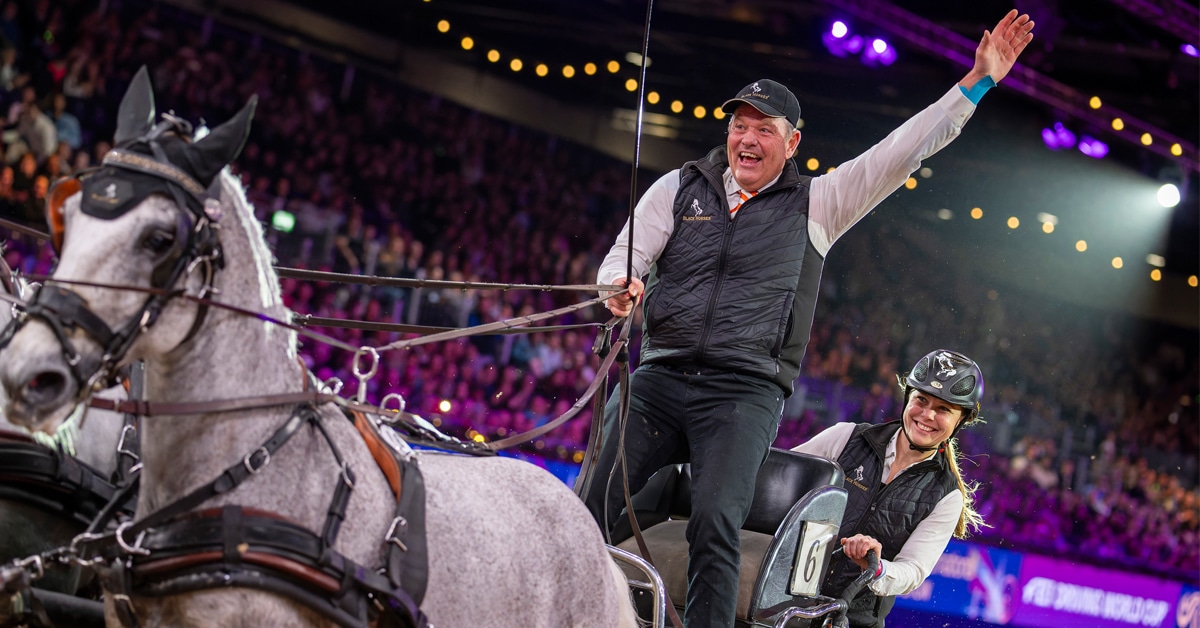 A smiling waving man driving a team of horses.
