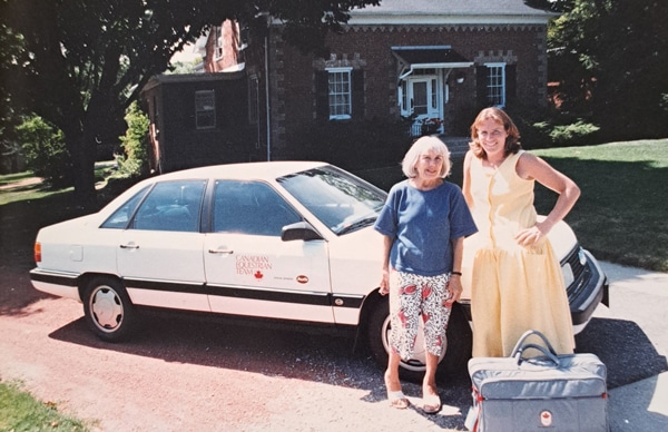 Two women standing beside a white car.